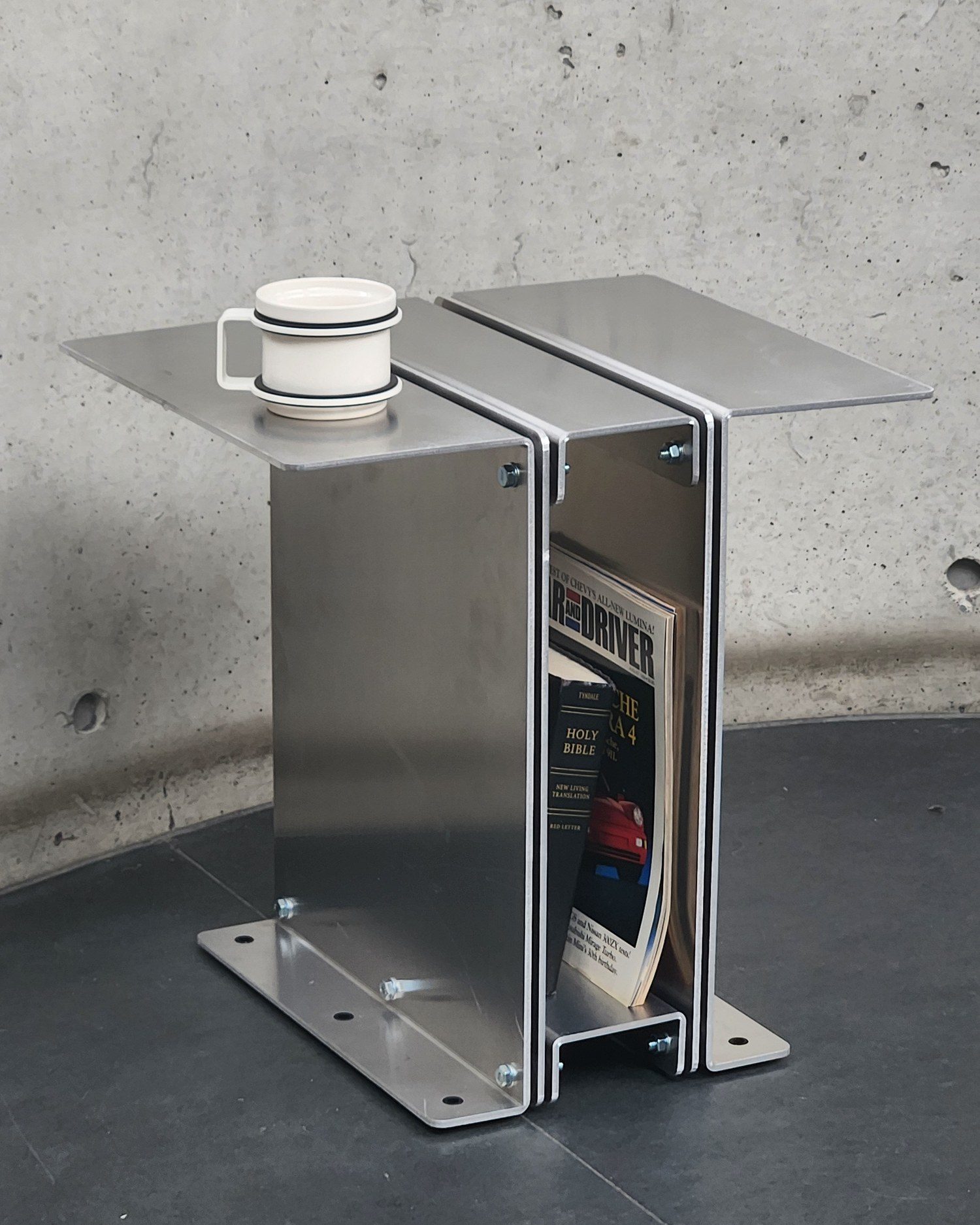 3082 Book Table against a concrete wall holding a magazine, with a mug on top